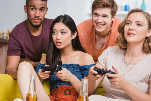 KYIV, UKRAINE - 28 JUILLET 2020 : des femmes excitées jouant à des jeux vidéo près d'amis multiculturels pendant la fête — Photo de stock