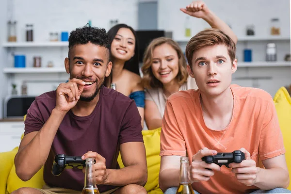 KIEW, UKRAINE - 28. JULI 2020: Selektiver Fokus einer aufgeregten Frau, die in der Nähe multiethnischer Freunde beim Videospiel Yeah-Geste zeigt — Stockfoto