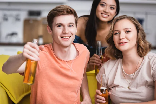 Enfoque selectivo de amigos multiculturales sosteniendo botellas de cerveza mientras mira la cámara - foto de stock