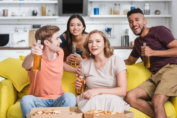 Amigos multiculturales emocionados con botellas de cerveza viendo películas durante la fiesta - foto de stock