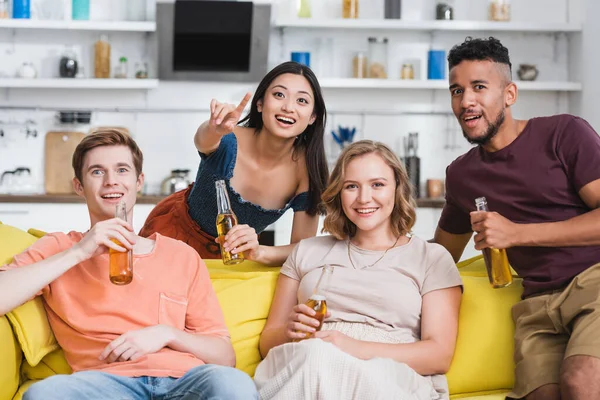 Eccitato donna asiatica che punta con il dito mentre guarda film con amici multietnici — Foto stock