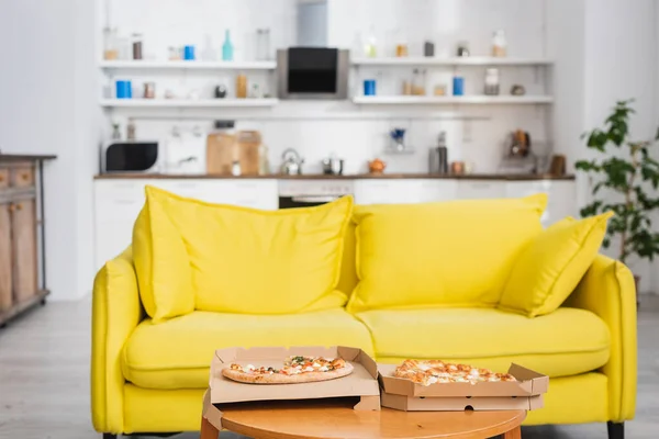 Deliciosa pizza na mesa perto de sofá amarelo na cozinha moderna — Fotografia de Stock