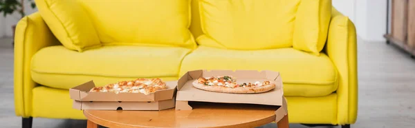 Récolte panoramique de délicieuses pizzas sur la table près du canapé jaune — Photo de stock