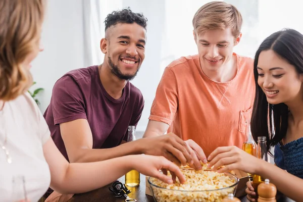 Foco seletivo de amigos multiculturais excitados tomando pipocas da tigela durante a festa — Fotografia de Stock