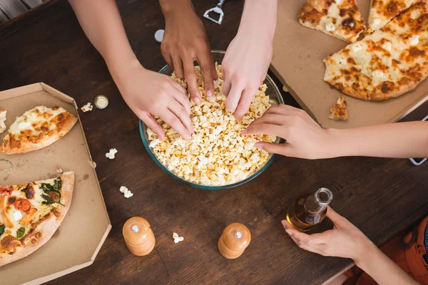 Blick von oben auf multikulturelle Freunde, die während der Party Popcorn aus der Schüssel holen, horizontale Ausrichtung — Stockfoto