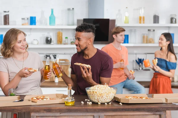 Multiethnische Freunde klirren während einer Party mit Bierflaschen und halten Pizza — Stockfoto