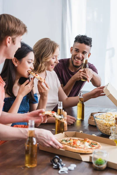 Aufgeregte multikulturelle Freunde, die während der Party Pizza essen und Bier trinken — Stockfoto