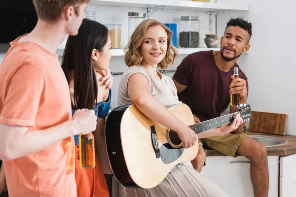 Selektiver Fokus der jungen Frau, die für fröhliche multikulturelle Freunde Gitarre spielt — Stockfoto