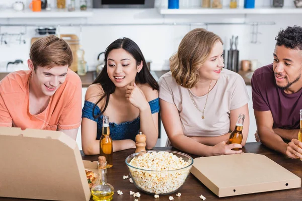 Amici multiculturali che parlano vicino a popcorn, birra e scatole di pizza durante la festa — Foto stock