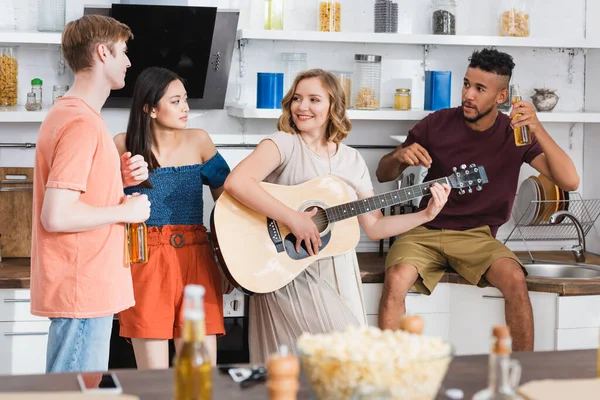 Foco seletivo de mulher alegre tocando guitarra para amigos multiculturais — Fotografia de Stock