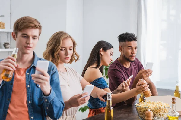 Вибірковий фокус молодих мультикультурних друзів спілкування на смартфонах біля пива і попкорну під час вечірки — стокове фото