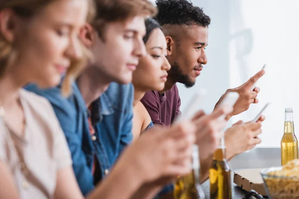 Selective focus of multiethnic friends messaging on smartphones during party — Stock Photo