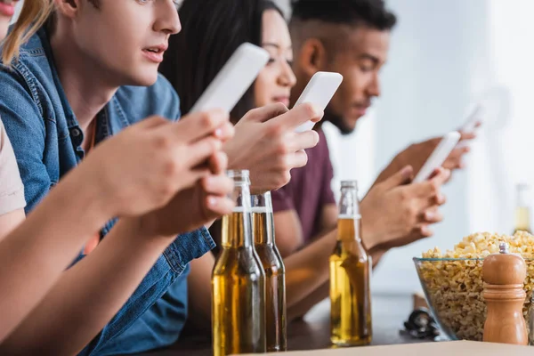 Selektiver Fokus multiethnischer Freunde, die während einer Party in der Nähe von Bier auf Smartphones chatten — Stockfoto