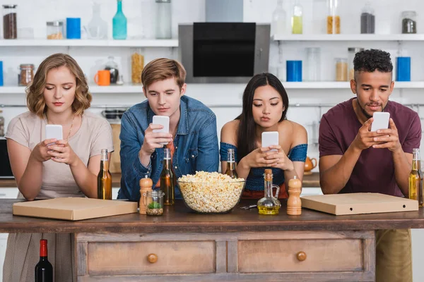 Мультикультурные друзья общаются по мобильным телефонам во время вечеринки возле пива и попкорна — стоковое фото