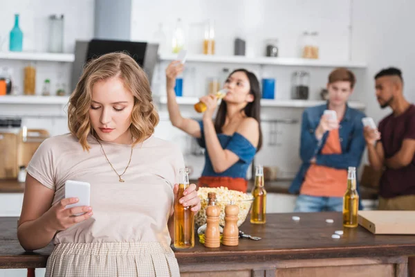 Selective focus of young woman chatting on smartphone near multicultural friends — Stock Photo