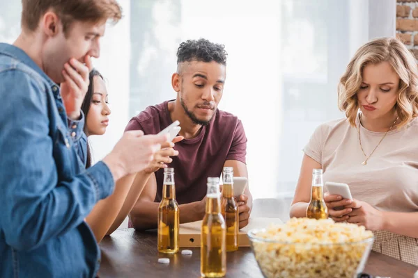 Вибірковий фокус багатоетнічних друзів спілкування на мобільних телефонах біля пива і попкорну під час вечірки — стокове фото