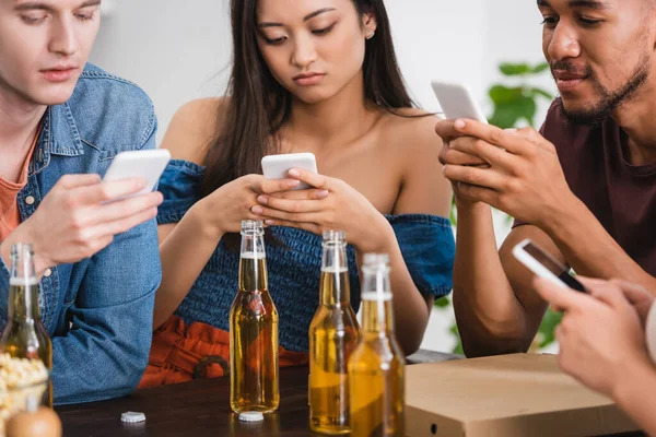 Selektiver Fokus multiethnischer Freunde, die während einer Party in der Nähe von Bier auf Smartphones chatten — Stockfoto