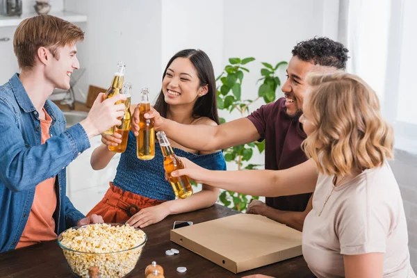 Excited multiethnic friends clinking bottles of beer during party — Stock Photo