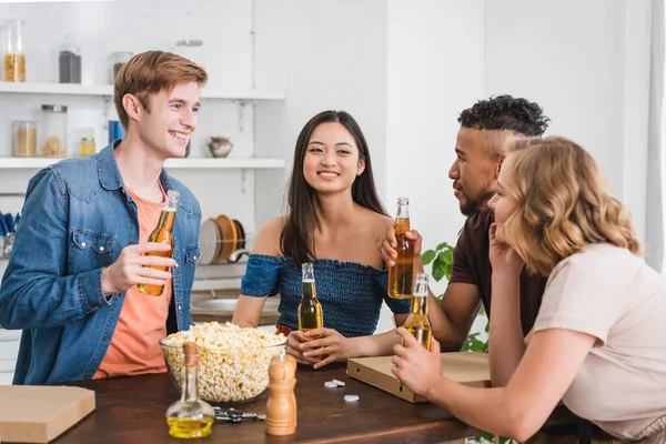 Amigos multiétnicos emocionados sosteniendo botellas de cerveza y hablando durante la fiesta - foto de stock