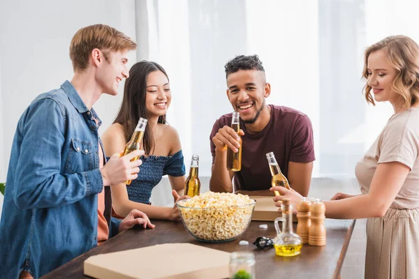 Selektiver Fokus fröhlicher multikultureller Freunde, die Flaschen Bier in der Hand halten und während der Party miteinander reden — Stockfoto