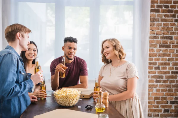 Joyful multicultural friends holding bottles of beer and talking during party — Stock Photo