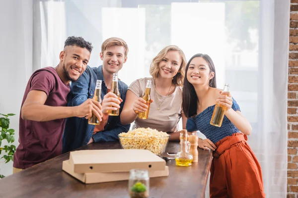 Fröhliche multiethnische Freunde blicken in die Kamera, während sie Bierflaschen in der Hand halten — Stockfoto