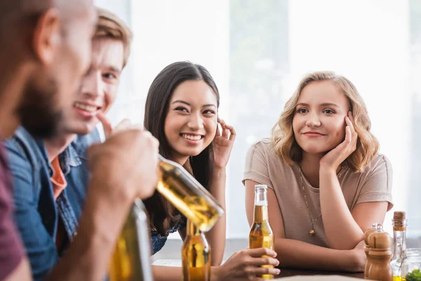 Enfoque selectivo de amigos multiculturales alegres con botellas de cerveza hablando durante la fiesta - foto de stock