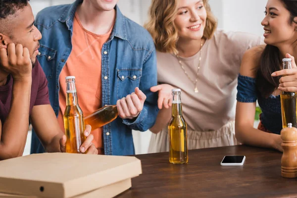 Selective focus of excited multicultural friends with bottles of beer talking during party — Stock Photo