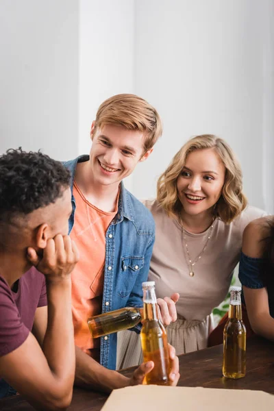 Multicultural friends talking near bottles of beer during party — Stock Photo