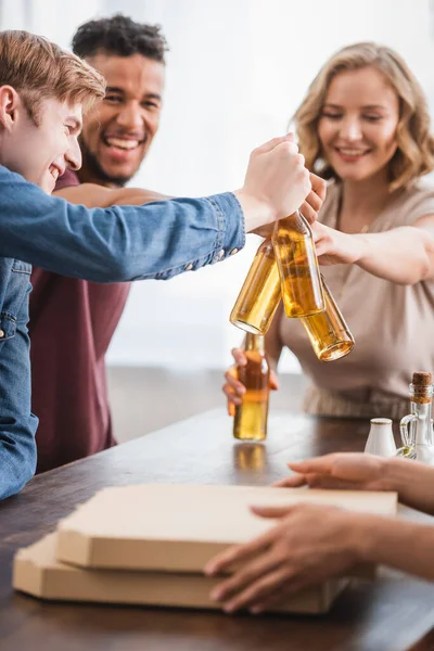 Messa a fuoco selettiva di amici multiculturali clinking bottiglie di birra durante la festa — Foto stock