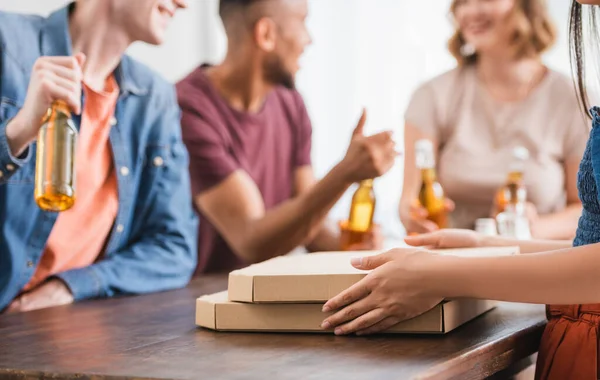 Vue recadrée de la femme près des boîtes à pizza et amis multiculturels avec de la bière sur fond — Photo de stock