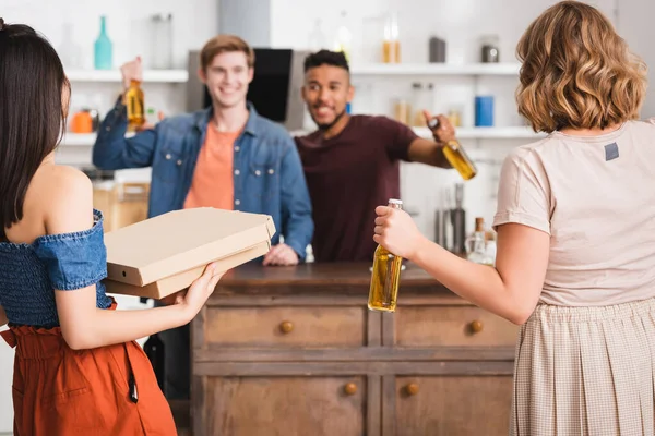 Vue arrière de femmes tenant des boîtes de bière et de pizza près d'hommes multiculturels — Photo de stock