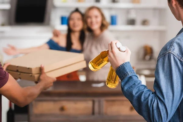 Foyer sélectif des hommes tenant des boîtes de bière et de pizza près des femmes multiculturelles sur fond — Photo de stock