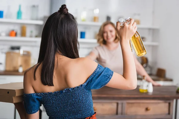 Espalda vista de morena mujer sosteniendo cerveza cerca amigo en fondo - foto de stock