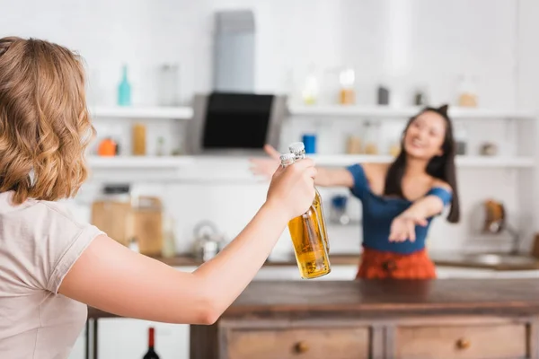 Selective focus of woman holding bottle of beer near friend in kitchen on background — Stock Photo