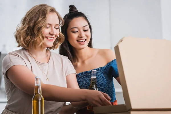 Excited multiethnic friends opening pizza box during party — Stock Photo
