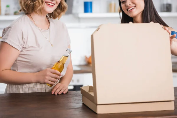Vista ritagliata di donna in possesso di bottiglia di birra vicino amico asiatico e scatola di pizza — Foto stock