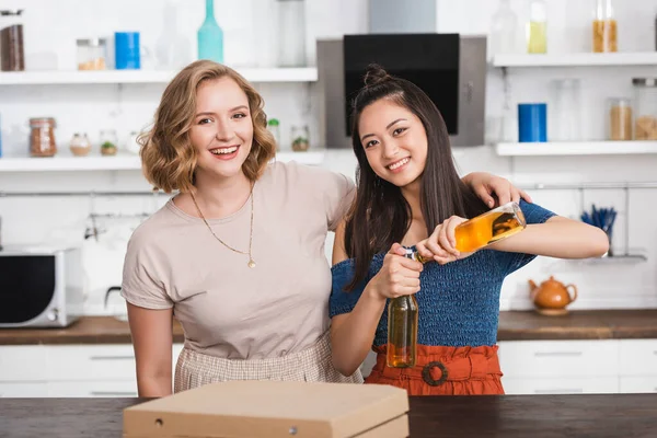 Excited asian woman opening bottles of beer near friends during party — Stock Photo