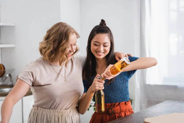 Joyful interracial friends opening bottles of beer during party — Stock Photo