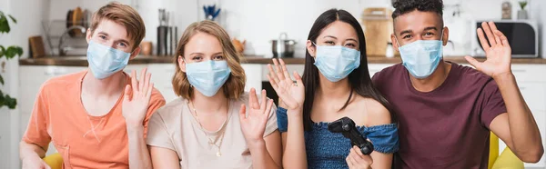 QUIIV, UCRÂNIA - JULHO 28, 2020: jovem asiática segurando joystick perto de amigos multiétnicos acenando as mãos em máscaras médicas — Fotografia de Stock