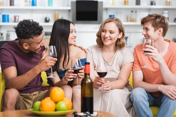 Багатоетнічні друзі дивляться один на одного, тримаючи окуляри червоного вина на кухні — стокове фото