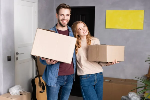 Joyful man and woman holding carton boxes in new home — Stock Photo