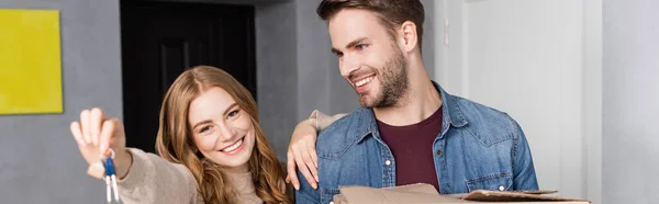 Panoramic crop of joyful woman holding keys near boyfriend — Stock Photo