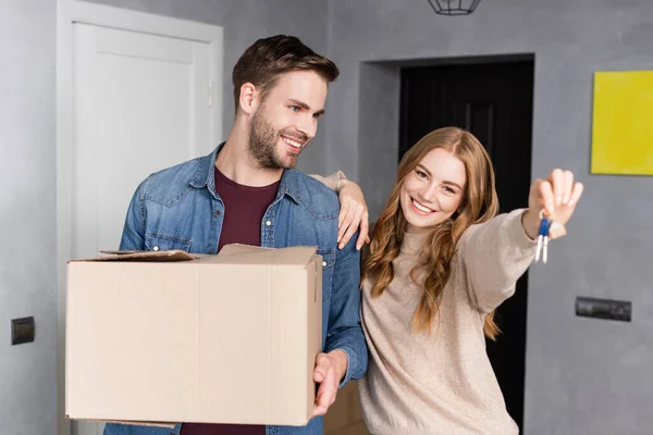 Mujer alegre sosteniendo llaves cerca de novio con caja — Stock Photo