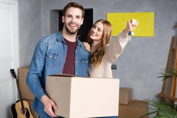 Frau mit Schlüssel und Blick auf freudigen Freund mit Schachtel, bewegendes Konzept — Stockfoto