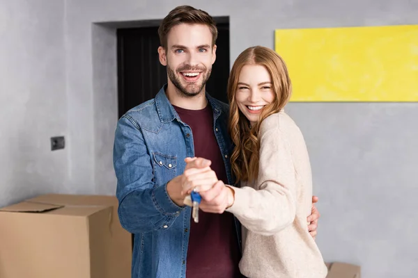 Hombre y mujer satisfechos tomados de la mano y las llaves cerca de la caja, concepto en movimiento - foto de stock