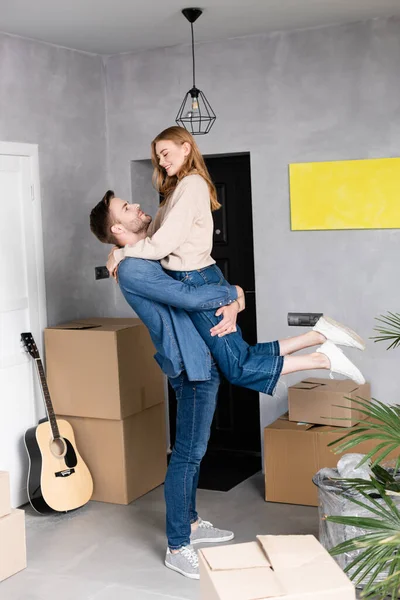 Mann im Arm erfreut Frau in der Nähe von Boxen und Akustikgitarre, Umzugskonzept — Stockfoto