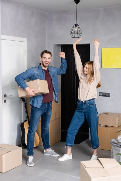 Excited man holding carton box near pleased woman standing with hands above head, relocation concept — Stock Photo