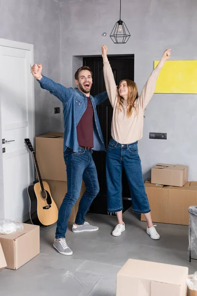 Excited couple standing with hands above head near carton boxes, relocation concept — Stock Photo
