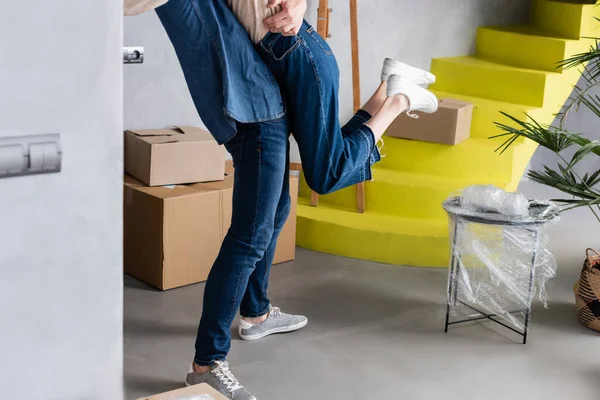 Vista recortada de la pareja abrazándose cerca de cajas de cartón y escaleras amarillas - foto de stock